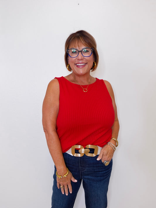 Woman wearing a red sleeveless top and blue jeans against a white background