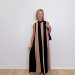 Woman wearing a sleeveless colorblock maxi dress in black and taupe stripe from THML against a white background. 