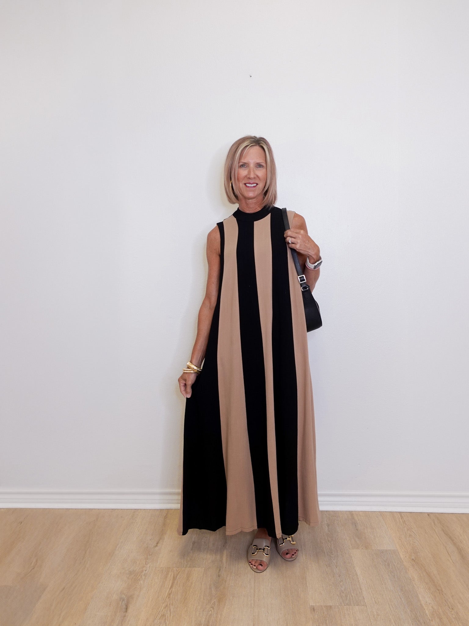 Woman wearing a sleeveless colorblock maxi dress in black and taupe stripe from THML against a white background. 