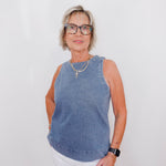 Woman wearing a blue sleeveless top and white pants against a plain background