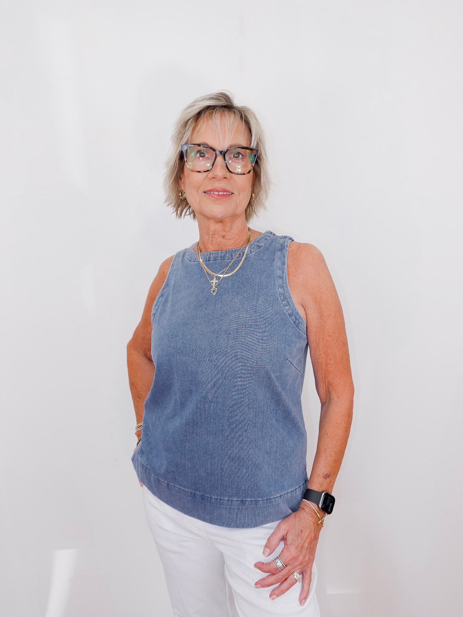 Woman wearing a blue sleeveless top and white pants against a plain background
