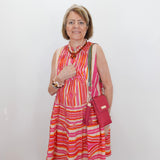 Woman wearing a colorful striped dress with a red handbag against a white wall.