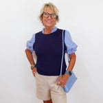 Woman wearing a navy sweater over a striped shirt with beige shorts and holding a blue clutch against a white background
