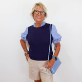 Woman wearing a navy sweater over a striped shirt with beige shorts and holding a blue clutch against a white background