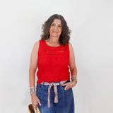Woman wearing a red sleeveless top and blue jeans against a white background
