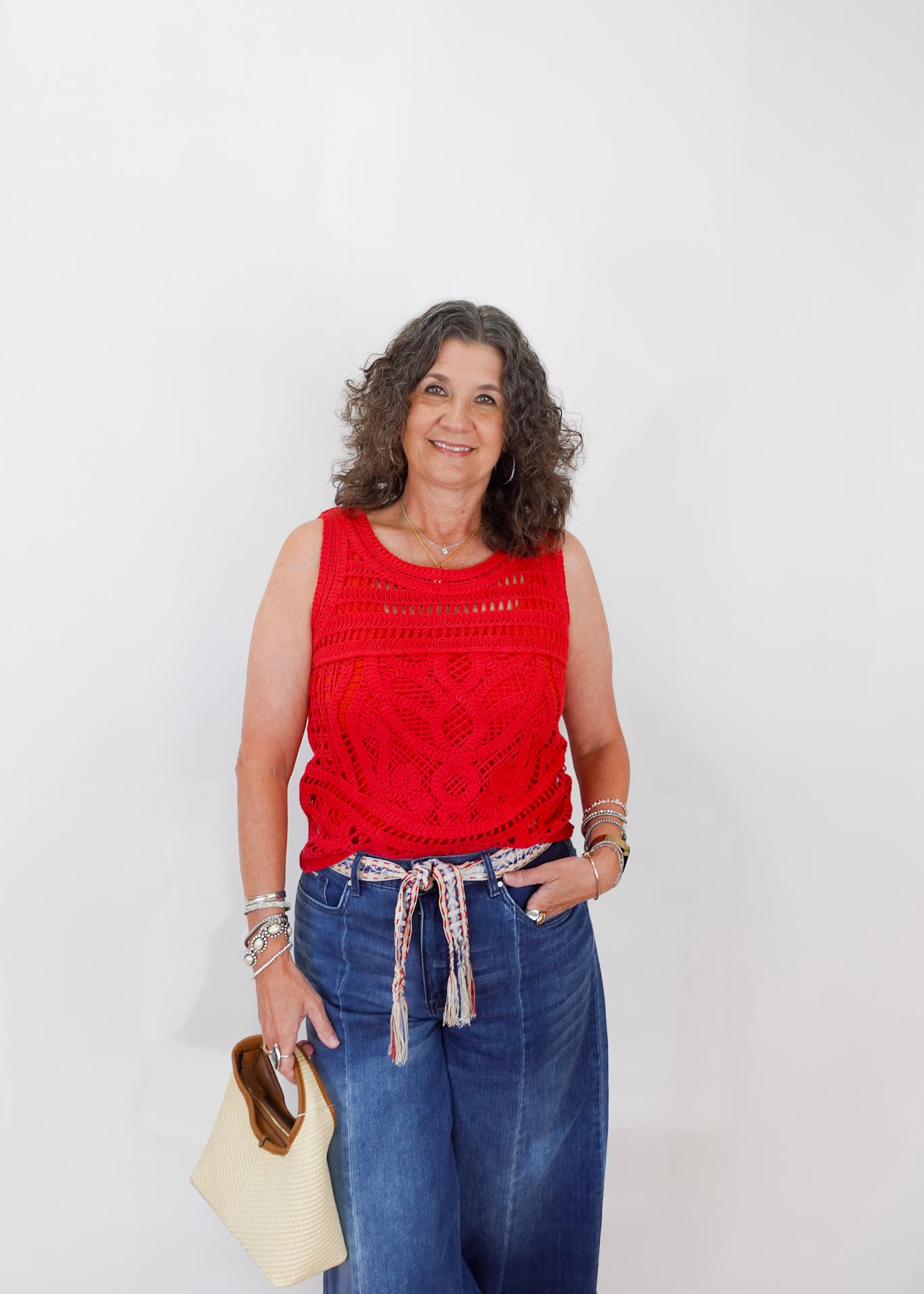 Woman wearing a red sleeveless top and blue jeans against a white background