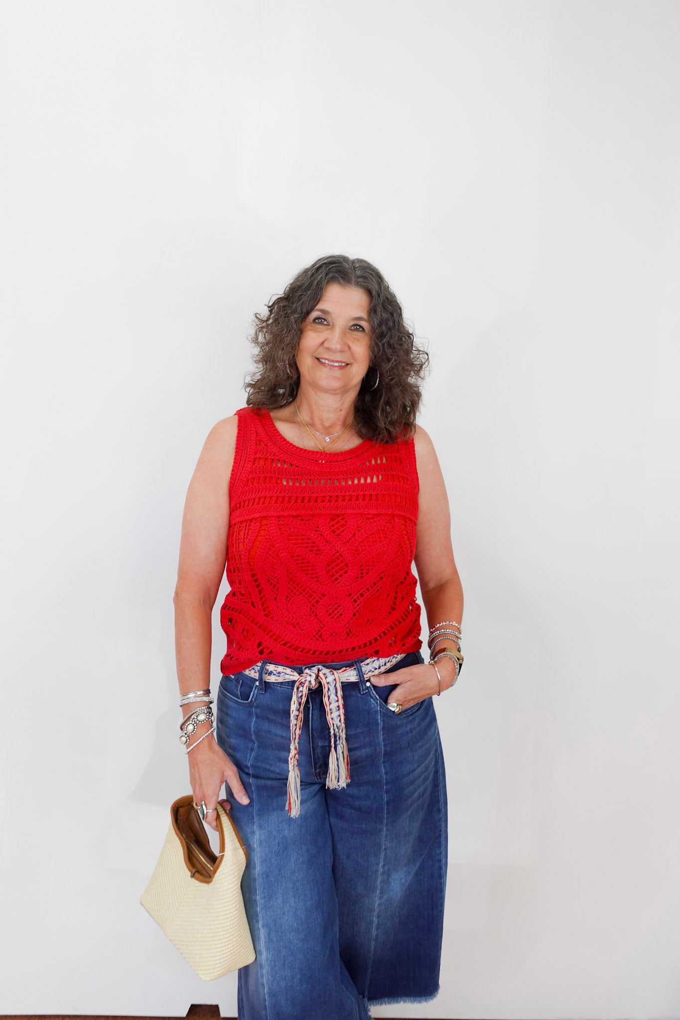 Woman wearing a red sleeveless top and blue jeans against a white background