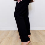 Person wearing black pants and beige sandals on a light wooden floor.