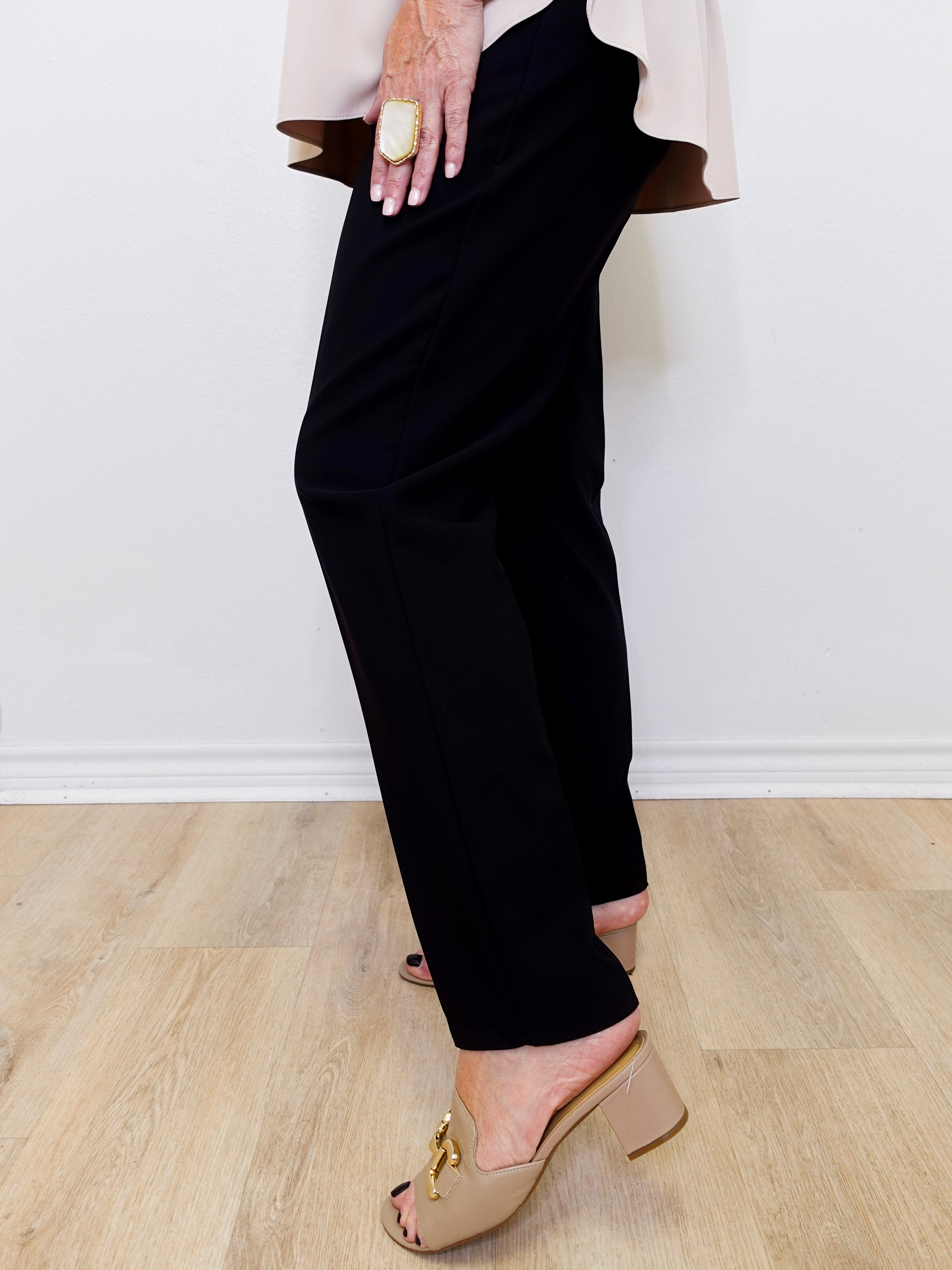 Person wearing black pants and beige sandals on a light wooden floor.