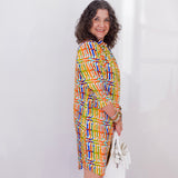 Woman wearing a colorful patterned dress holding a white bag against a white background