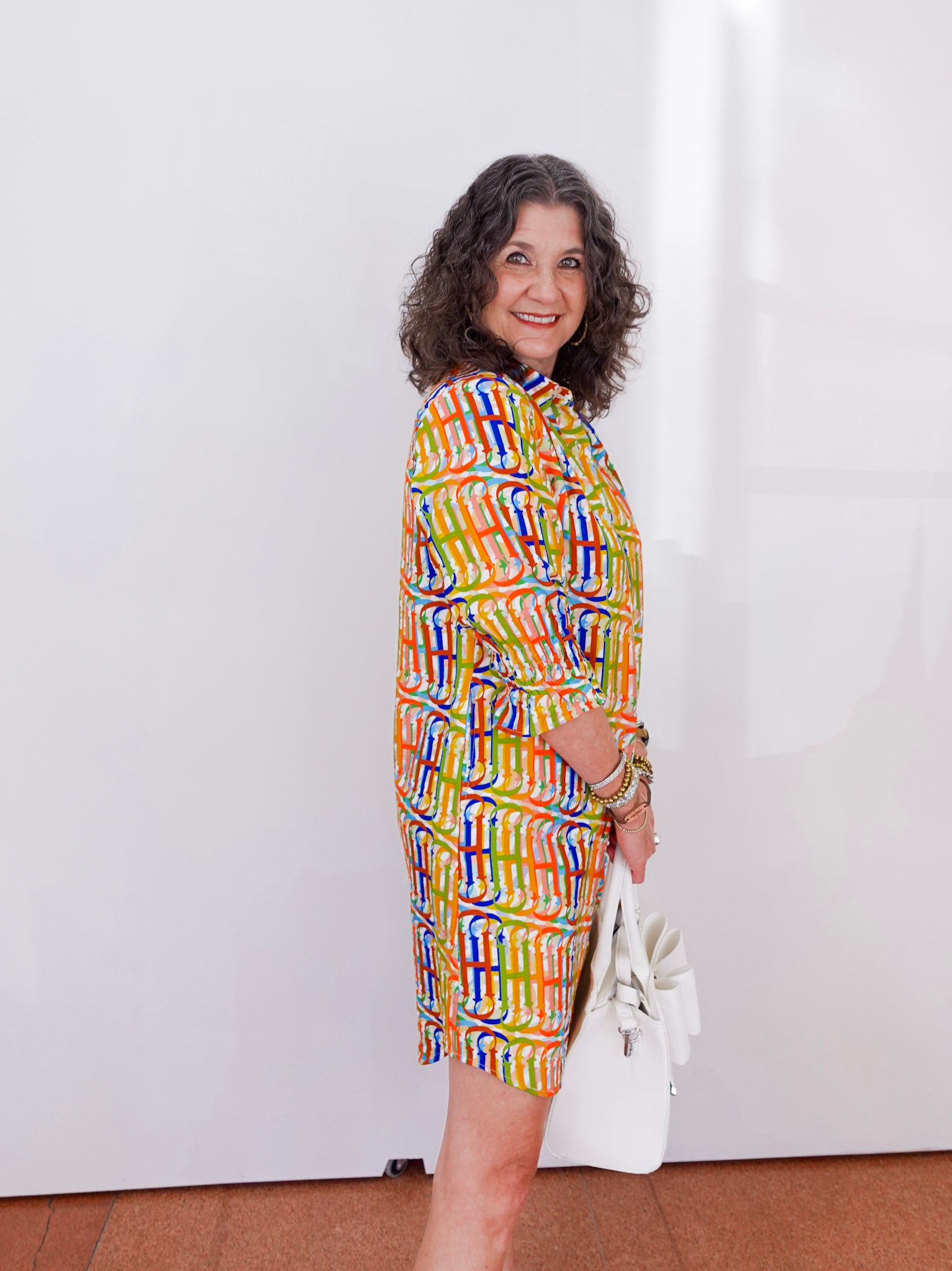 Woman wearing a colorful patterned dress holding a white bag against a white background