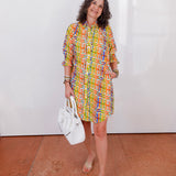 Woman in a colorful dress holding a white handbag against a plain background