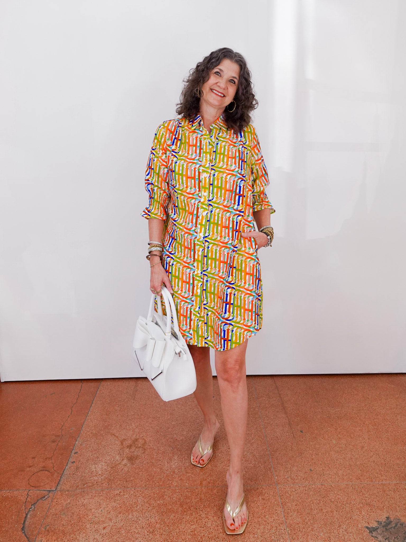 Woman in a colorful dress holding a white handbag against a plain background