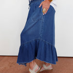 Person wearing a blue denim skirt with ruffled hem on a plain background