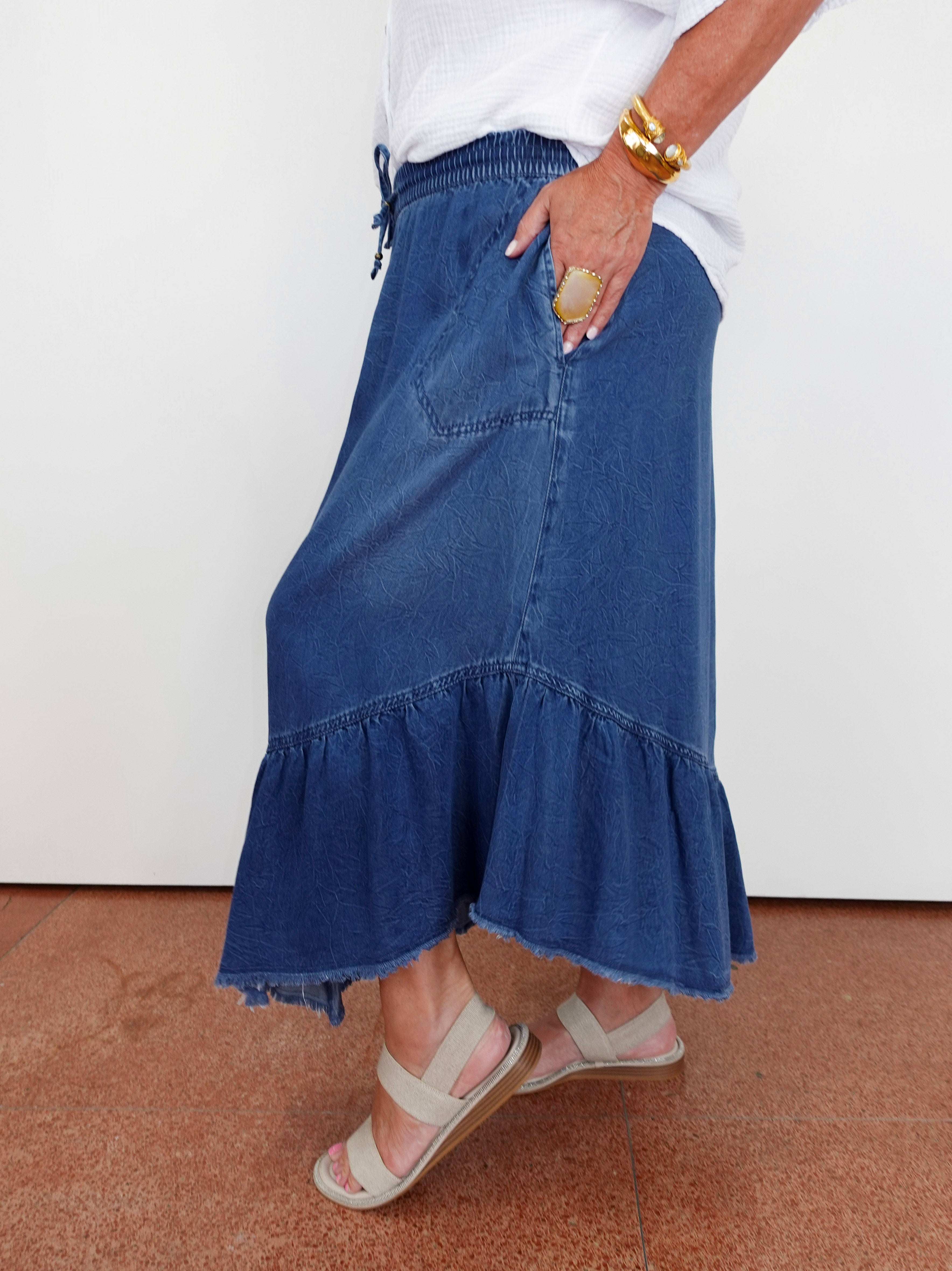 Person wearing a blue denim skirt with ruffled hem on a plain background