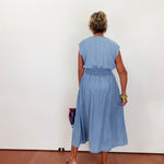 Person wearing a blue dress standing against a white wall.