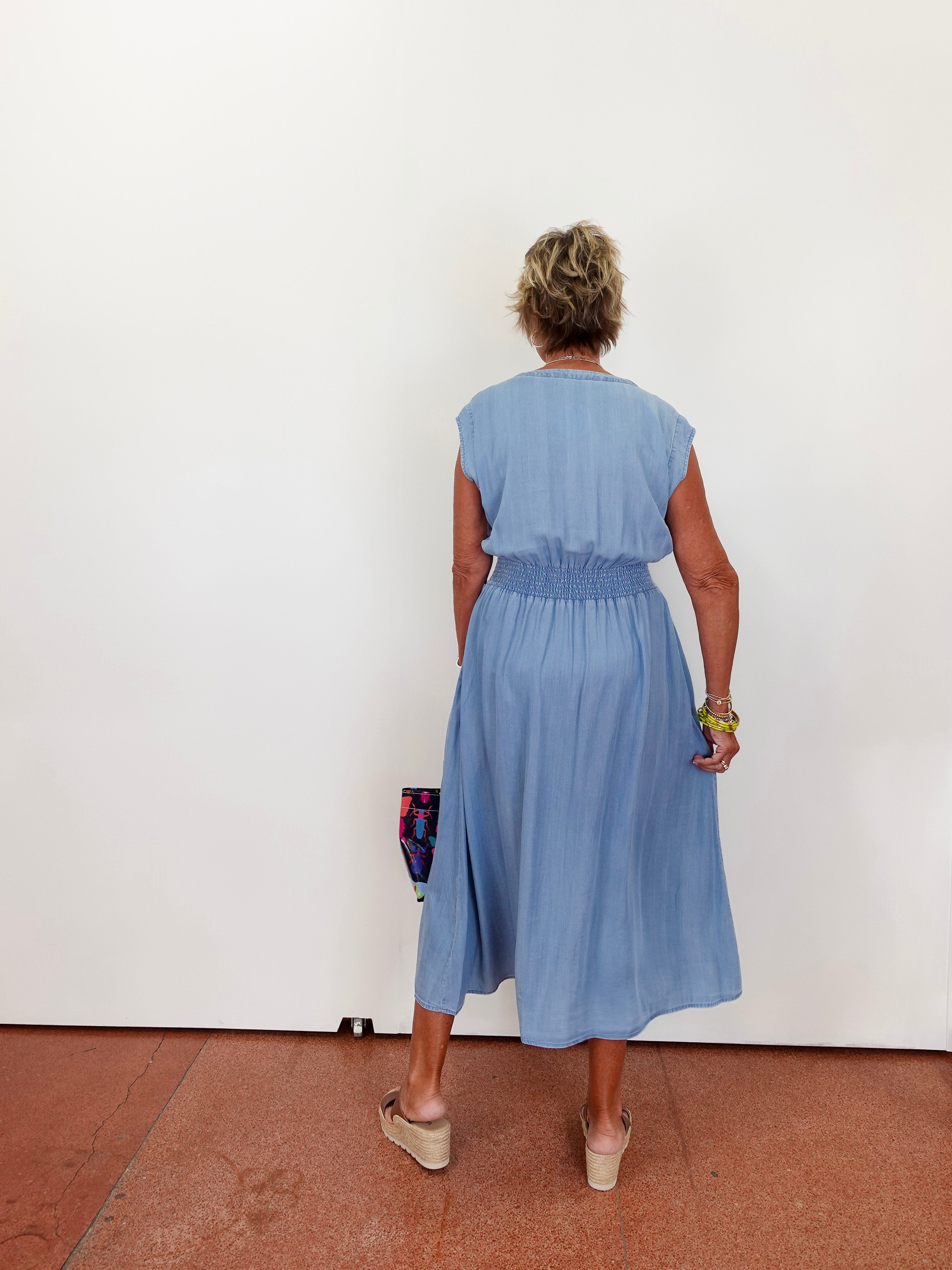 Person wearing a blue dress standing against a white wall.