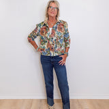 Woman wearing a floral shirt and jeans standing against a white wall.