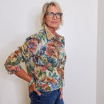 Woman wearing a floral blouse and glasses against a white wall