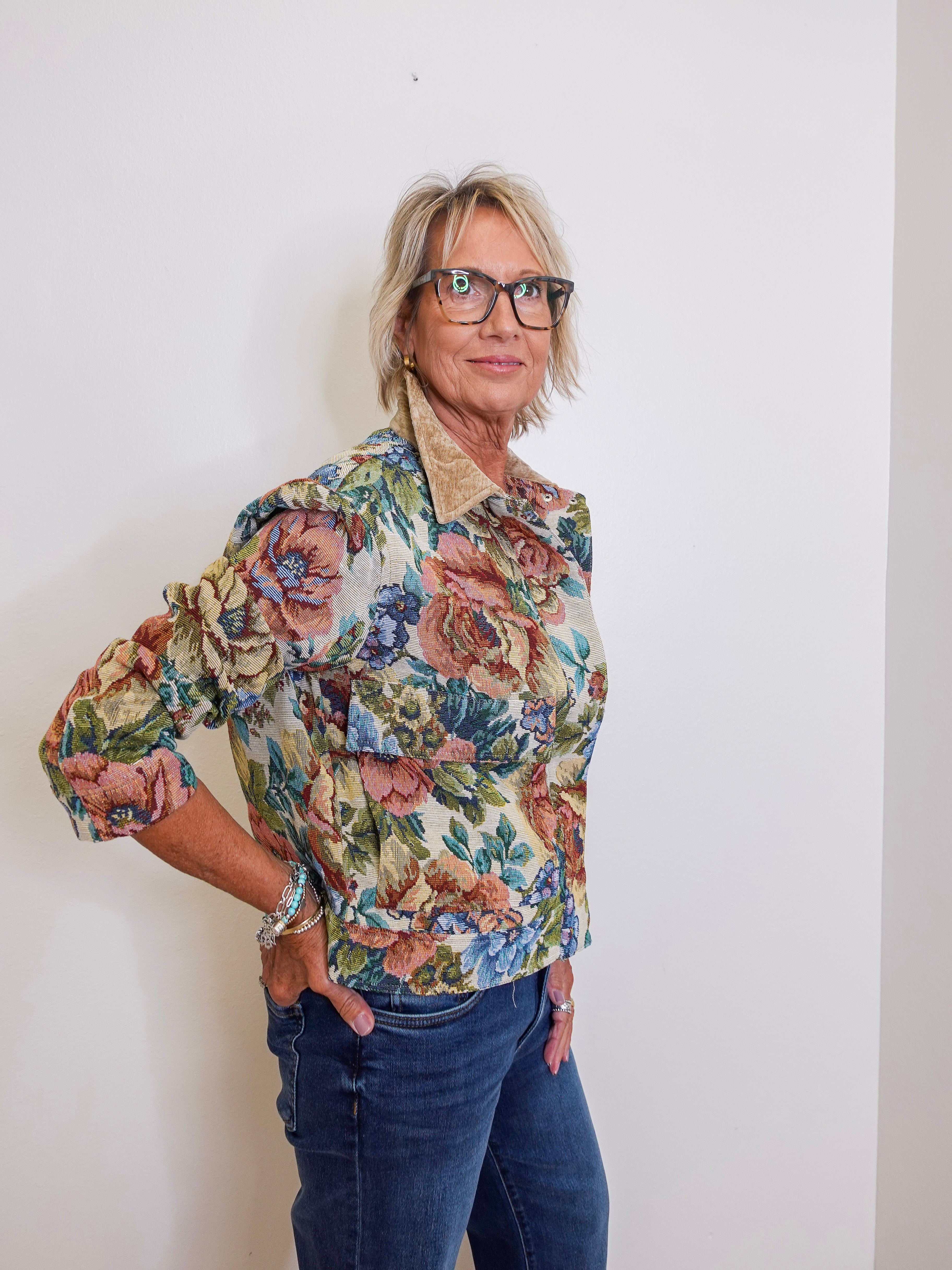 Woman wearing a floral blouse and glasses against a white wall