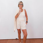 Woman in a white outfit standing against a plain white wall.