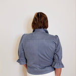 Person wearing a blue jacket with ruffled sleeves on a white background
