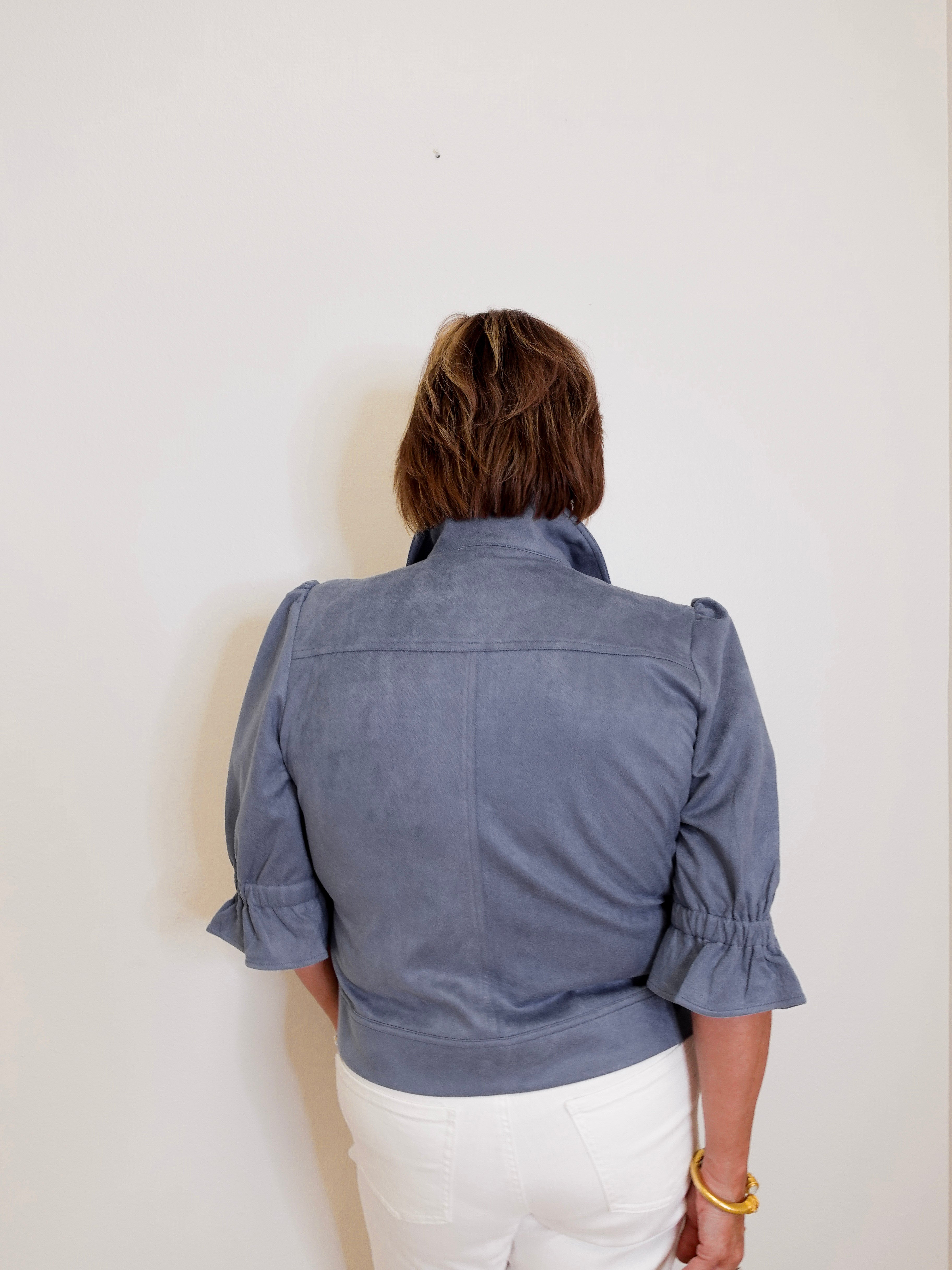 Person wearing a blue jacket with ruffled sleeves on a white background
