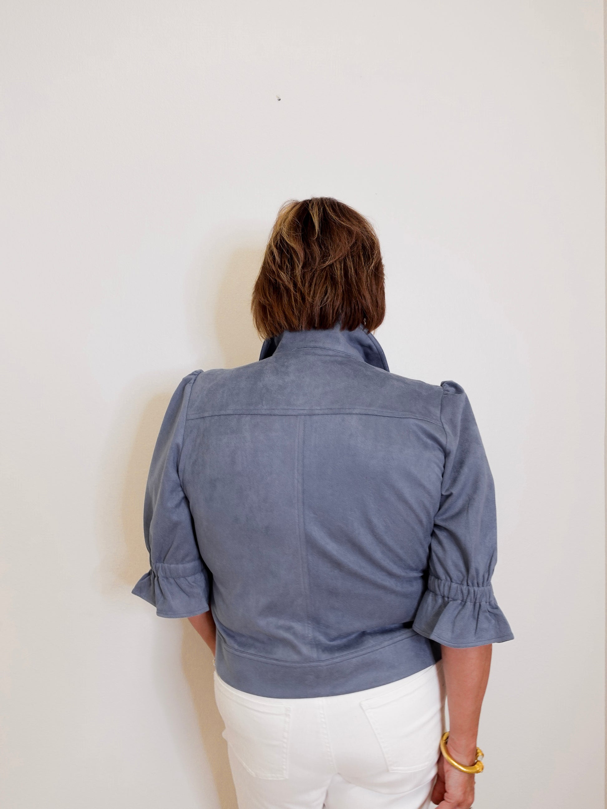 Person wearing a blue jacket with ruffled sleeves on a white background