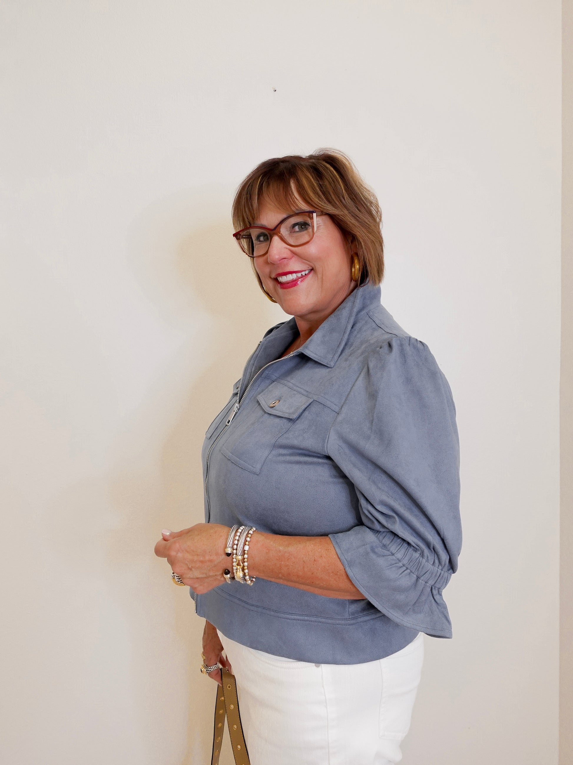 Woman wearing a gray jacket and white pants against a plain background