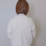 A person wearing a white crop cardigan with long sleeves against a white background. 
