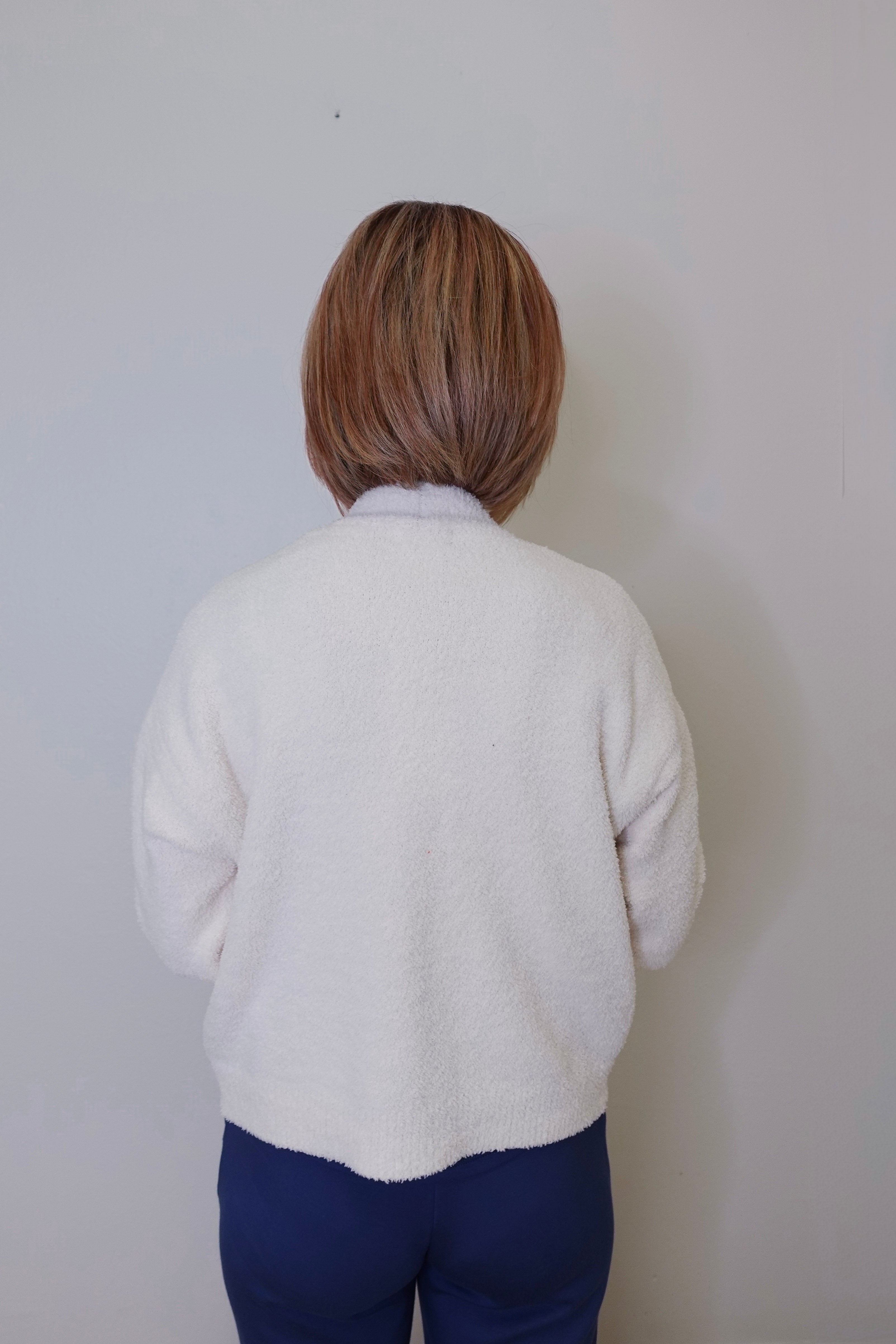 A person wearing a white crop cardigan with long sleeves against a white background. 