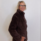 Person wearing a brown jacket and glasses against a white wall