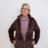 Woman wearing a brown fleece jacket and purple pants against a white background