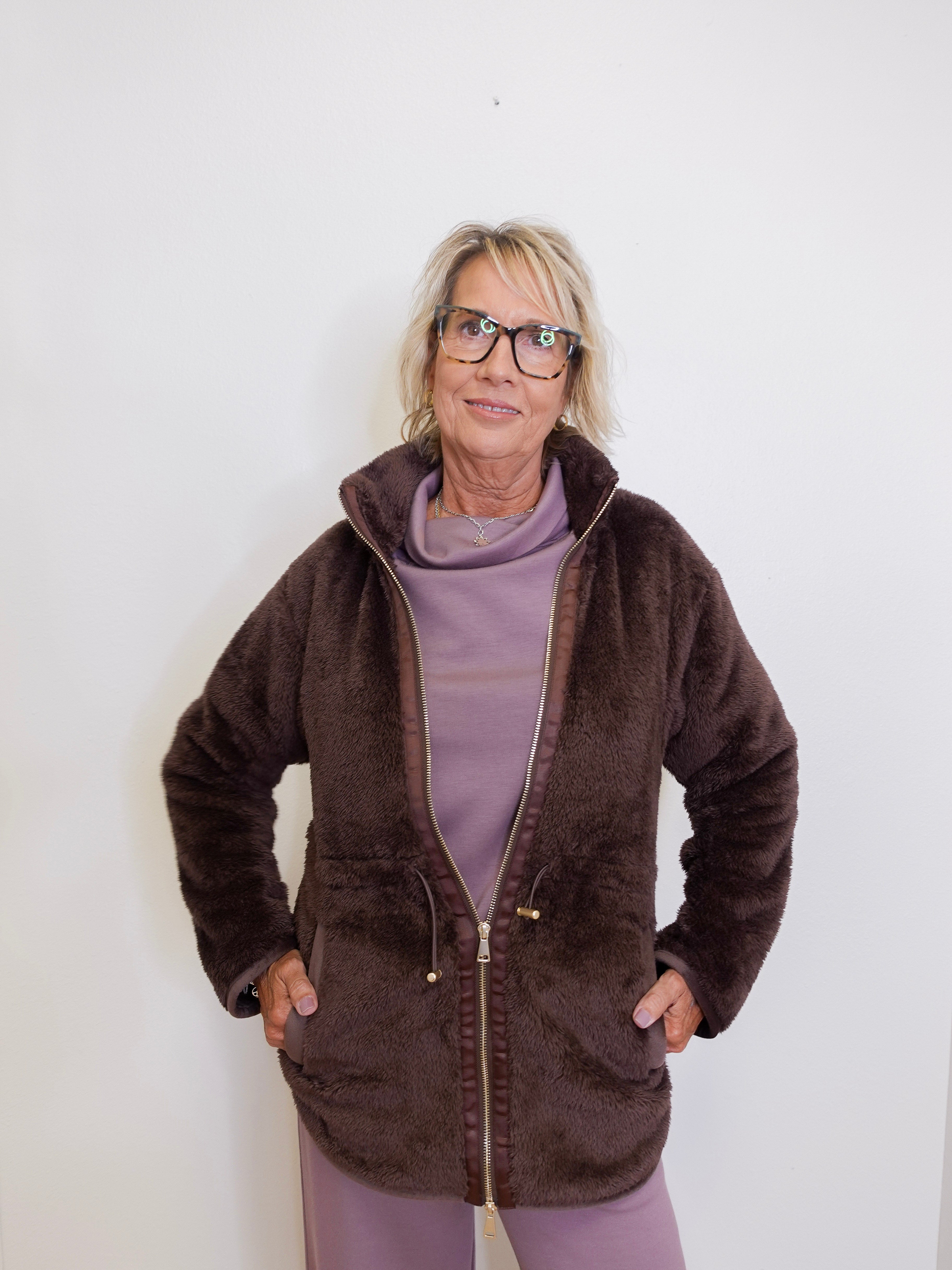 Woman wearing a brown fleece jacket and purple pants against a white background