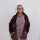 Person wearing a brown jacket and purple outfit against a white background