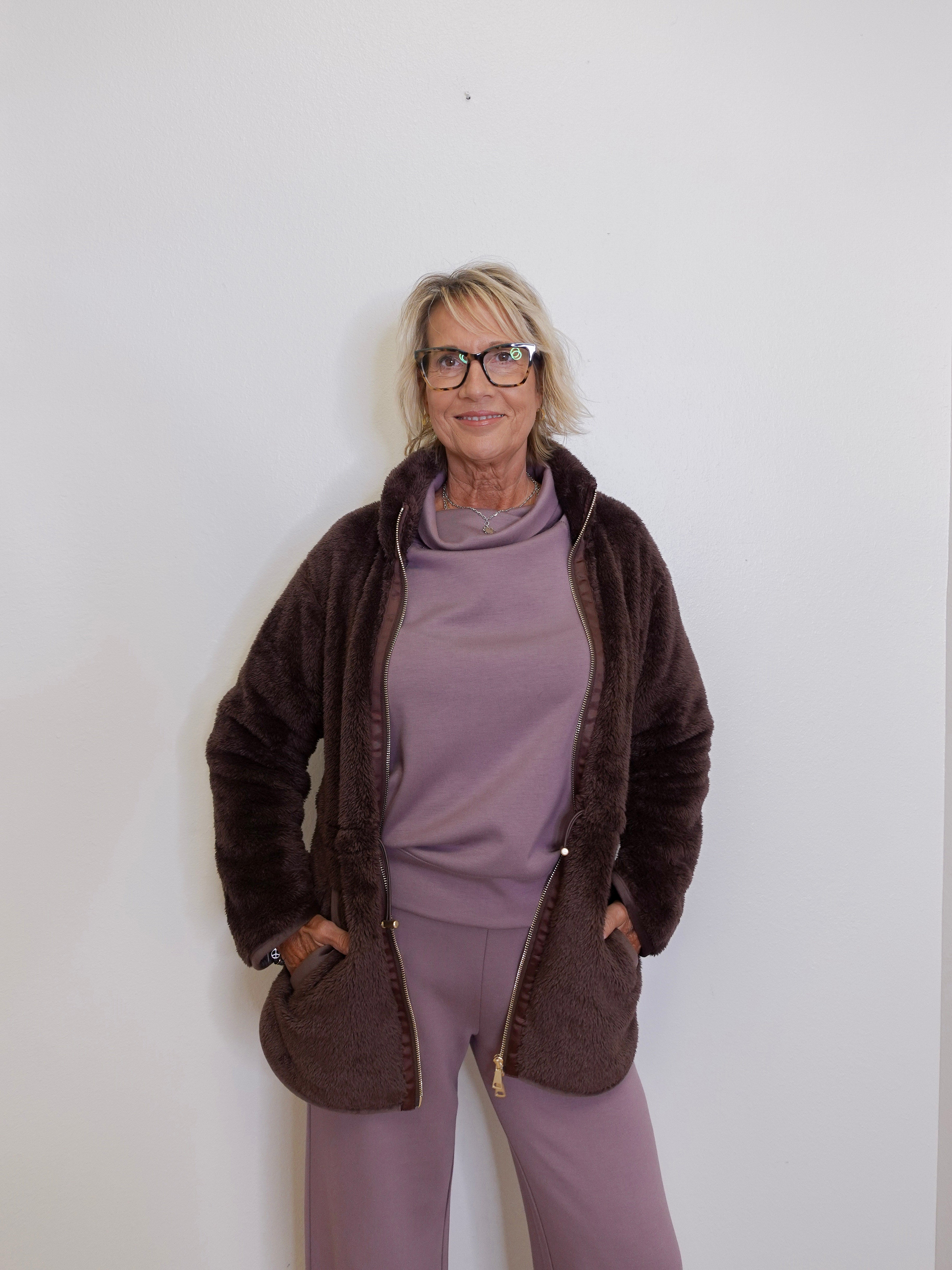 Person wearing a brown jacket and purple outfit against a white background