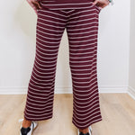 Person wearing a striped outfit with wide-leg pants against a white wall.
