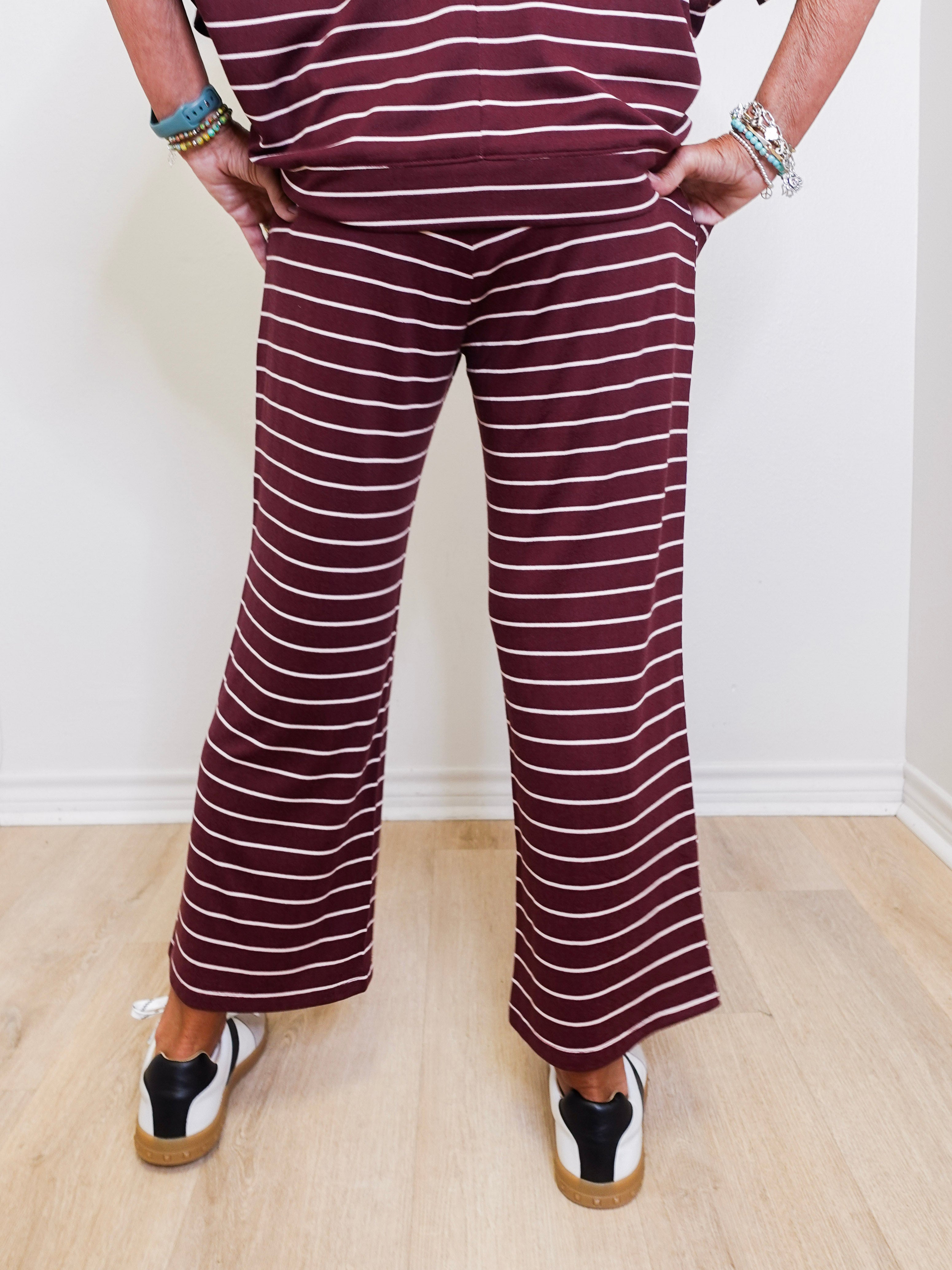 Person wearing a striped outfit with wide-leg pants against a white wall.