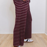 Person wearing maroon and white striped pants with white sneakers on a light wooden floor.