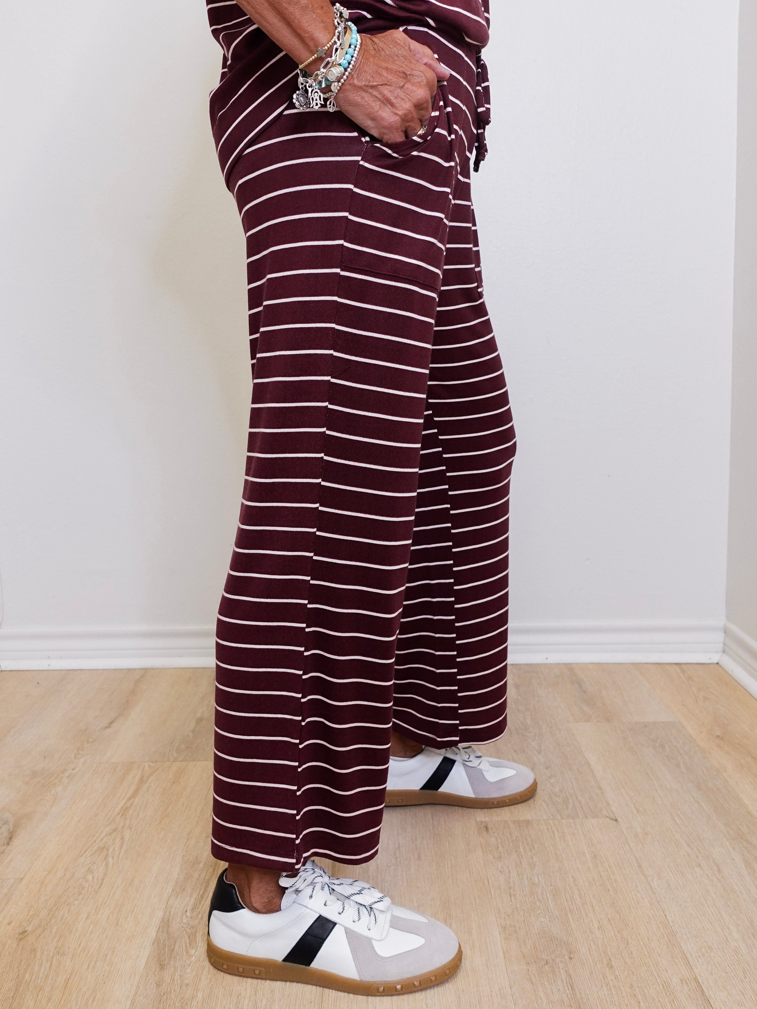 Person wearing maroon and white striped pants with white sneakers on a light wooden floor.