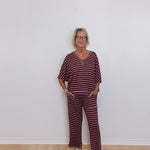 Woman wearing a maroon and white striped outfit standing against a white wall.
