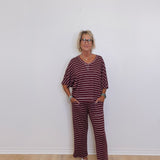 Woman wearing a maroon and white striped outfit standing against a white wall.