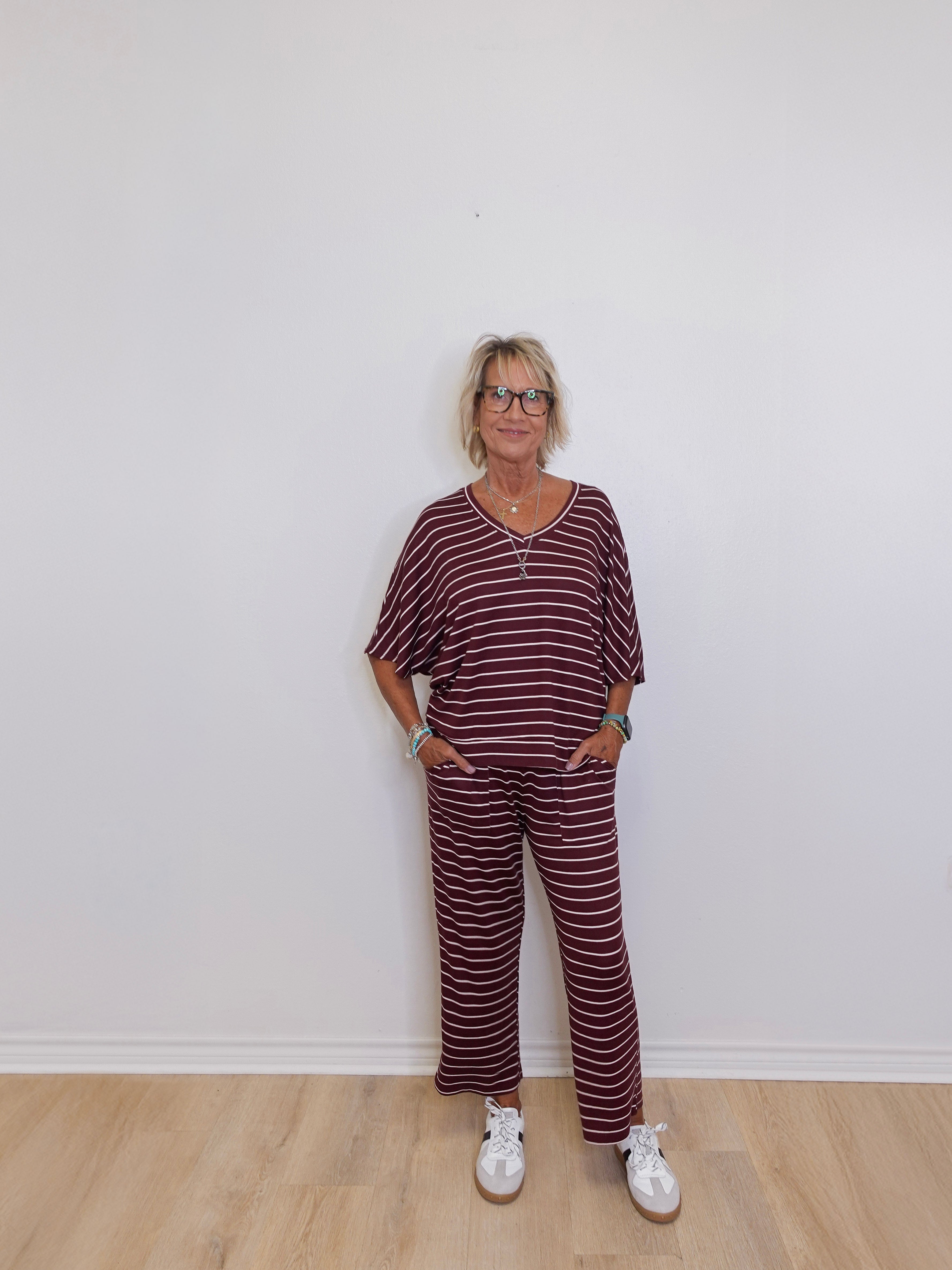 Woman wearing a maroon and white striped outfit standing against a white wall.