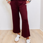 Person wearing a burgundy outfit with white sneakers on a light wooden floor.