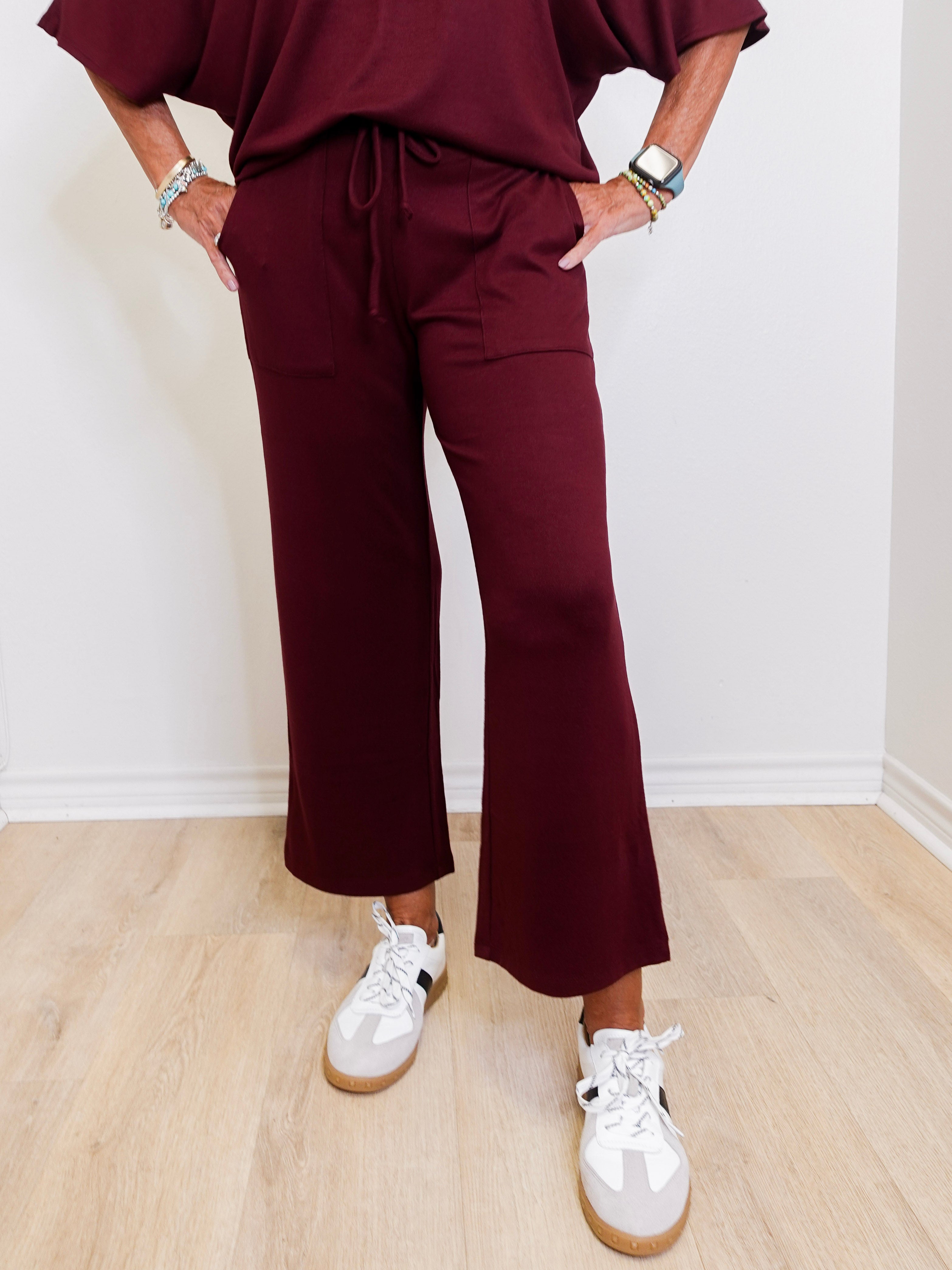Person wearing a burgundy outfit with white sneakers on a light wooden floor.