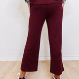 Person wearing a burgundy outfit with wide-leg pants on a light wooden floor.