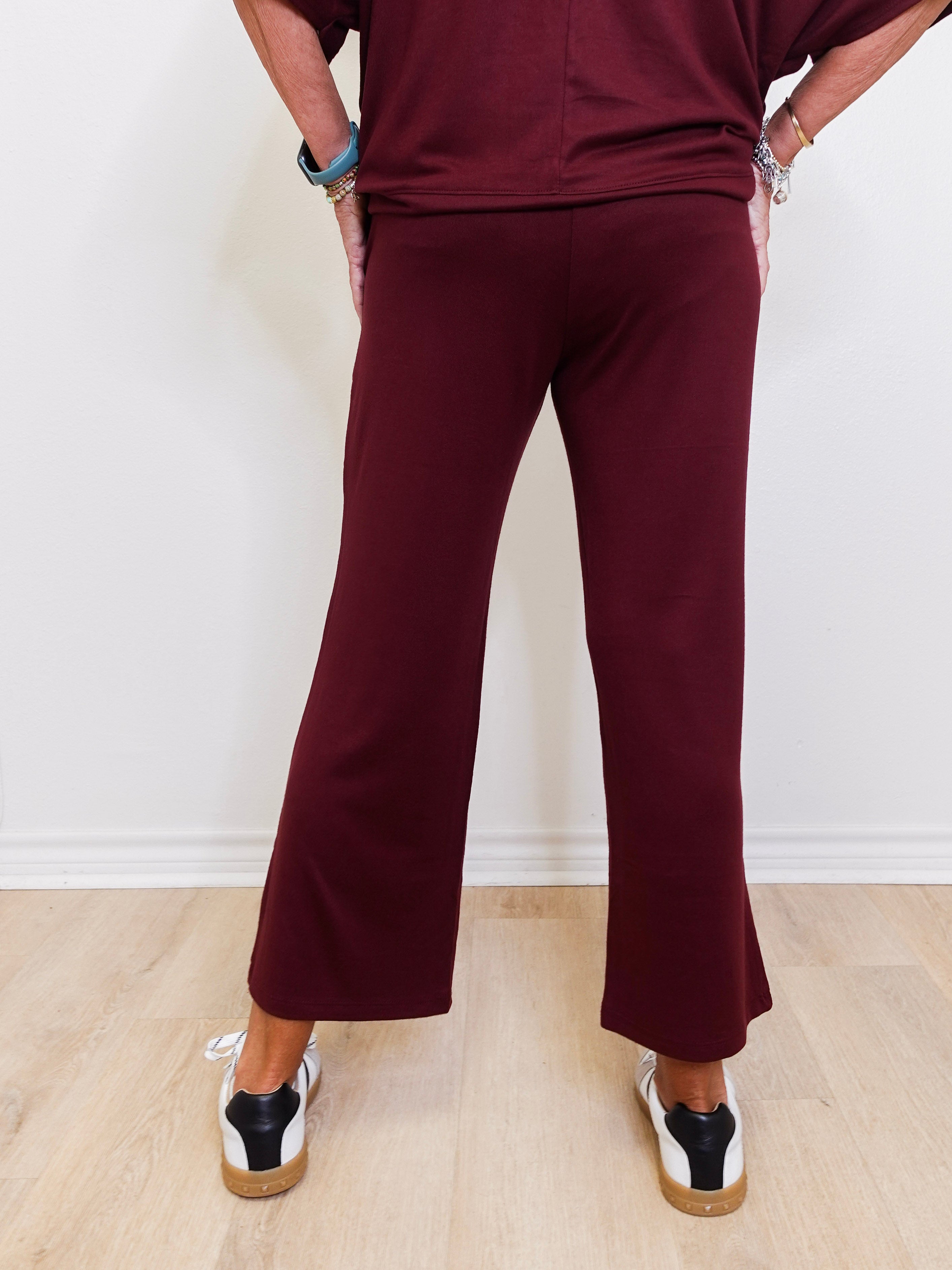 Person wearing a burgundy outfit with wide-leg pants on a light wooden floor.