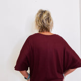 Person wearing a burgundy oversized shirt against a white wall