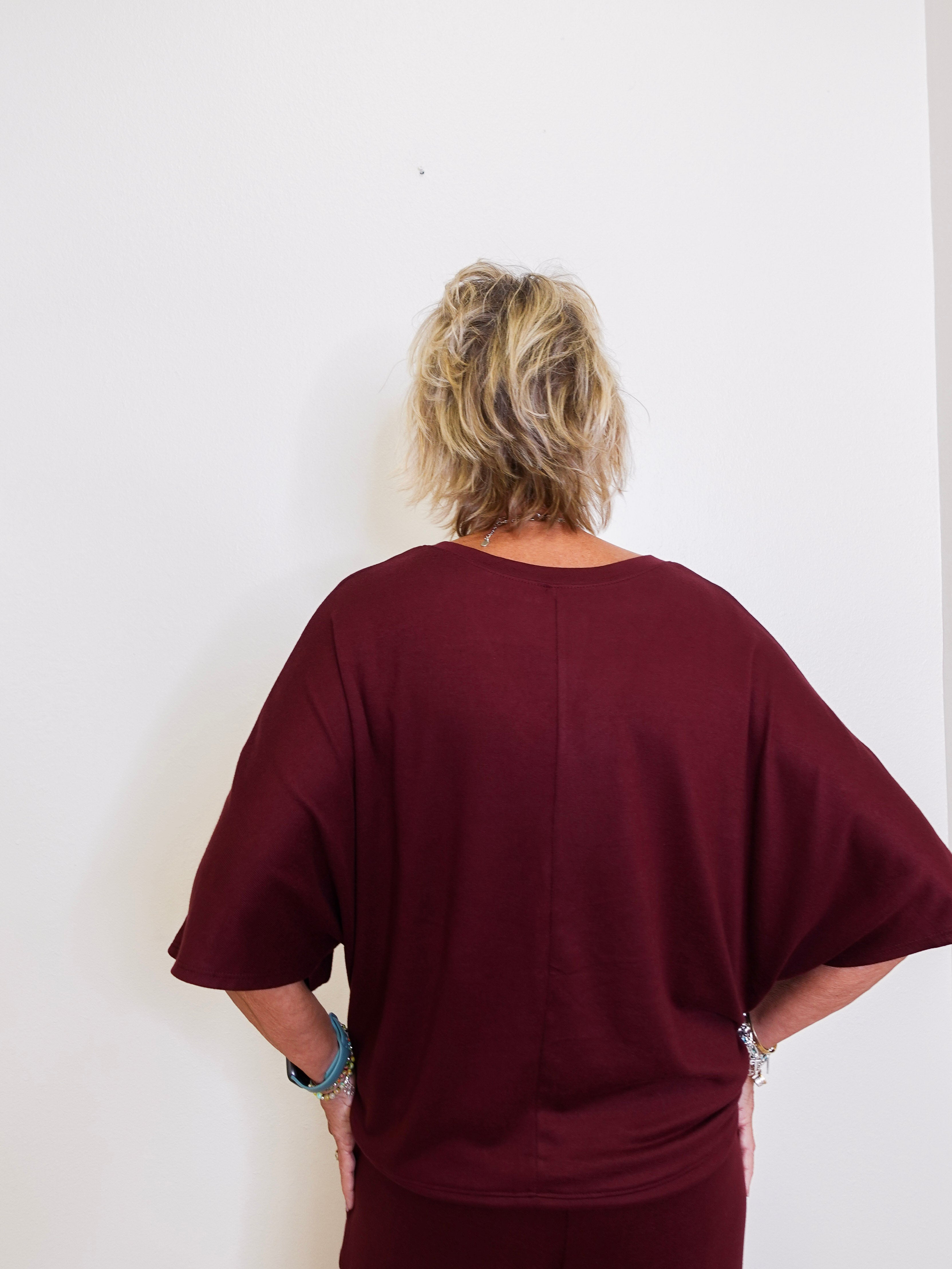 Person wearing a burgundy oversized shirt against a white wall