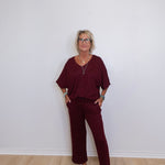 Woman wearing a burgundy outfit with white sneakers against a plain white wall.
